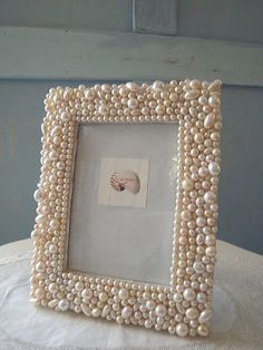 a white frame with pearls on it sitting on top of a cloth covered tablecloth