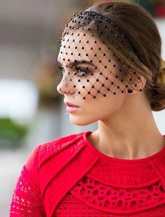 a woman wearing a red dress with a black netted veil on top of her head