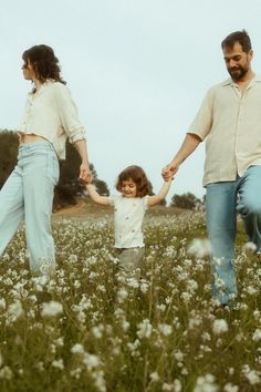 two adults and a child walking through a field with flowers on the ground in front of them