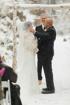 the bride and groom are getting married under an arbor in the snow at their wedding ceremony