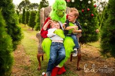 two children are sitting on a chair in the middle of christmas trees with an adult monster behind them