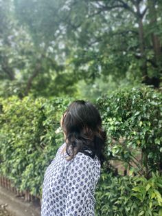 a woman standing in front of a hedge with her back to the camera and looking up