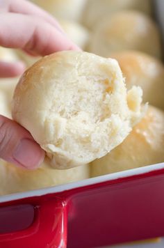 a hand holding a biscuit over a red pan filled with buns and rolls