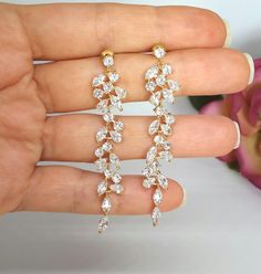 a woman's hand holding two pairs of diamond earring sets in yellow gold