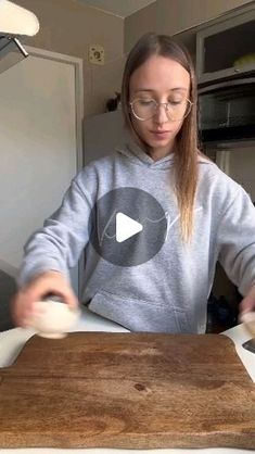 a woman in glasses is making something on a cutting board while another person looks at the camera