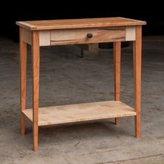 a small wooden table with one drawer on the top and two shelves below it, sitting in an empty room