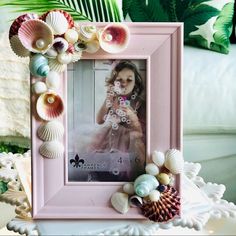 a pink frame with shells and seashells around it on a table next to a white couch