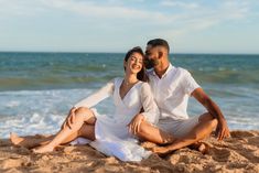 a man and woman are sitting on the sand at the beach, posing for a photo