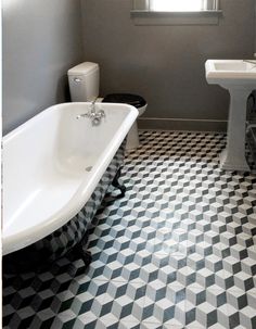 a white bath tub sitting next to a toilet and sink in a bathroom with black and white flooring