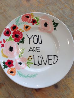 a white plate with flowers painted on it that says you are loved in black lettering