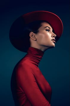 a woman in a red dress and hat with her head turned to the side looking up