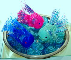 two plastic fish sitting in a bowl filled with blue, pink and green water bottles