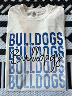 Get this popular new Bulldogs stacked text shirt and show off your school spirit in style!  Each shirt is printed in-house by me using high-quality materials on a Comfort Colors shirt, known for its exceptional comfort, style, and durability. Available in unisex sizes S to 3X, and youth sizes, we've got you covered regardless of your preferred fit. The Bulldogs stacked text Shirt features a classic crew neck and short sleeves, making it suitable for year-round wear. The flattering silhouette ensures a comfortable and stylish fit for both men and women. Please note that ivory is ONLY available in Adult sizes!  Note: As each shirt is individually printed, slight variations in color and placement may occur, adding to the uniqueness and charm of your Preppy Bulldogs Shirt. Your shirt will come Cheap Letter Print Tops For School Spirit, Long Sleeve Cheer Shirts, Bulldog Volleyball Shirts, Middle School Spirit Wear, School Mascot Shirt Designs, Cheap School Spirit Shirt For Game Day, School Spiritwear Ideas, Sublimation School Spirit Shirts, Cheap School Spirit Shirt With Funny Text