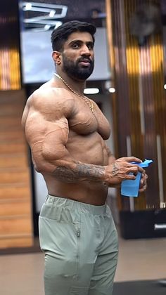 a shirtless man holding a blue bottle in his right hand and looking at the camera