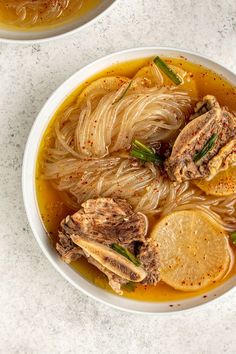 two bowls filled with noodles and meat on top of a white countertop next to each other