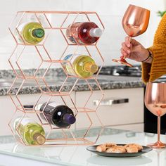 a woman is holding a wine glass in her hand and standing next to a rack with several bottles on it