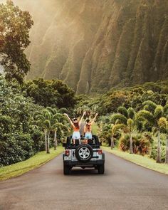 three people are riding in the back of a pick up truck on a country road