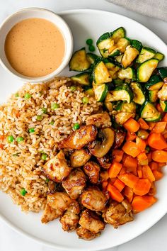 a white plate topped with rice and veggies next to a cup of sauce