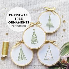 three christmas tree ornaments with gold ribbon and thread on the table next to some spools of thread