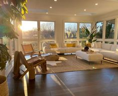 a living room filled with white furniture and large windows overlooking the trees in the distance