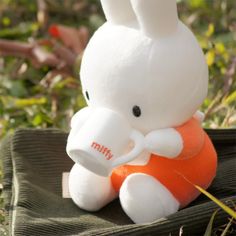 a white stuffed rabbit sitting on top of an orange pillow in the grass with it's legs crossed