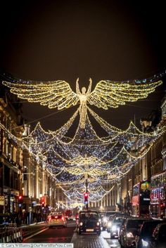 an angel statue is lit up in the middle of a busy city street at night