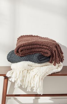 three blankets stacked on top of each other on a wooden bench in front of a white wall