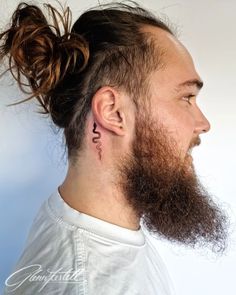 a man with long hair and a beard has a tattoo on his left side of the ear