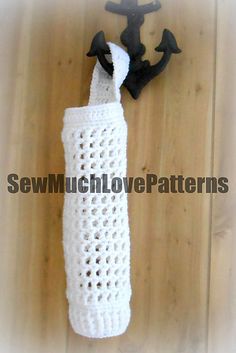 a white crocheted bottle cover with black handles on a wooden floor next to an iron hook