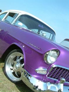 an old purple car parked on top of a grass covered field next to a white truck