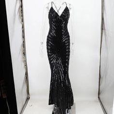 a black evening gown on display in a glass case with white walls and curtains behind it