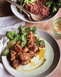 two bowls filled with meat and garnish next to a glass of water on a wooden table