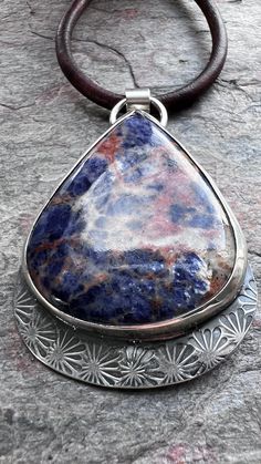 I have set a large Sodalite cabochon in sterling and fine silver. The natural stone is accented by a hand stamped sterling silver backplate. The silver has been oxidized and polished to create its antiqued patina finish. This one-of-a-kind pendant hangs from a genuine leather cord. The end of the cord features a sterling silver clasp and a 5-inch extender chain allowing it to be worn from 25-30 inches. Be sure to see all photos and video for size and color reference. Sodalite: 37x45mm Handmade Pendant Necklace, Patina Finish, Statement Pendant, Sterling Silver Necklace Pendants, Fantasy Jewelry, Silver Pendant Necklace, Handmade Pendants, Sterling Silver Pendant, Fine Silver