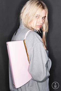 a woman with blonde hair holding a pink handbag in front of her face and looking at the camera