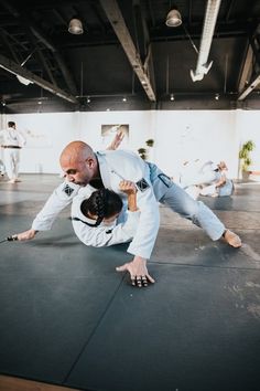 two men in white shirts and black pants are practicing martial moves on a mat with one man holding the other