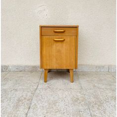 a small wooden cabinet sitting on top of a cement floor next to a white wall