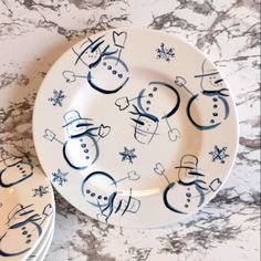 two plates with snowmen on them sitting on a marble counter top next to each other