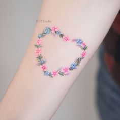 a woman's arm with pink and blue flowers in the shape of a heart