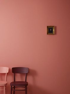 two chairs against a pink wall with a painting on the wall behind them and a small chair in front of it