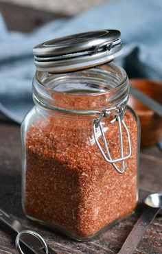 a jar filled with red sand next to scissors and spoons on a wooden table