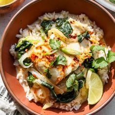 a bowl filled with rice and vegetables on top of a table next to lemon wedges