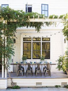 an outdoor dining table and chairs on a porch with greenery in the foreground