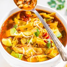 a white bowl filled with vegetable soup and a spoon on top of the bowl next to it