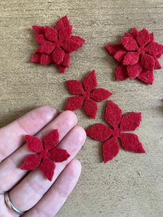 someone is holding their hand over some felt flowers that are red and they look like petals