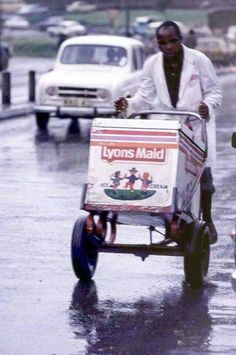 a man pushing a cart down the street in the rain with an advertisement on it