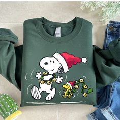 a green shirt with a snoopy christmas hat on it next to jeans and cactus