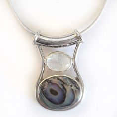 Paua Shell and Rainbow Moonstone have always been the perfect pairing! Colorful swirls throughout the shell match the flashes in the Rainbow Moonstone! This pendant is just over 1" long and will come with a sterling Silver Chain! It was designed by Marianna and Richard and handmade by the Artisans of Bali!  The pendant is being sold by the designers themselves! Silver Necklace With Large Round Stone, Silver Jewelry With Natural Stones And Mother Of Pearl, Silver Mother Of Pearl Necklace With Gemstone, Colorful Swirls, Iridescent Moonstone Pendant Jewelry, Handmade Sterling Silver Shell-shaped Necklace, Nickel-free Moonstone Pendant Jewelry, Rainbow Moonstone Necklace, Rainbow Moonstone Pendant