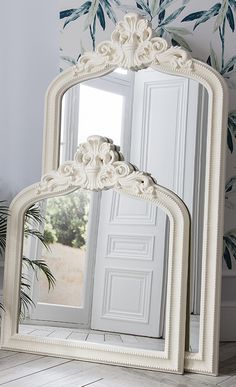 a white mirror sitting on top of a wooden floor next to a potted plant