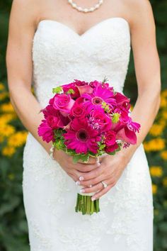 a woman in a wedding dress holding a bouquet of pink and purple flowers with pearls