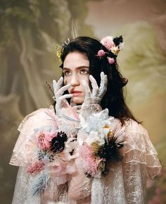 a woman with flowers on her head and hands in front of her face, wearing a white dress